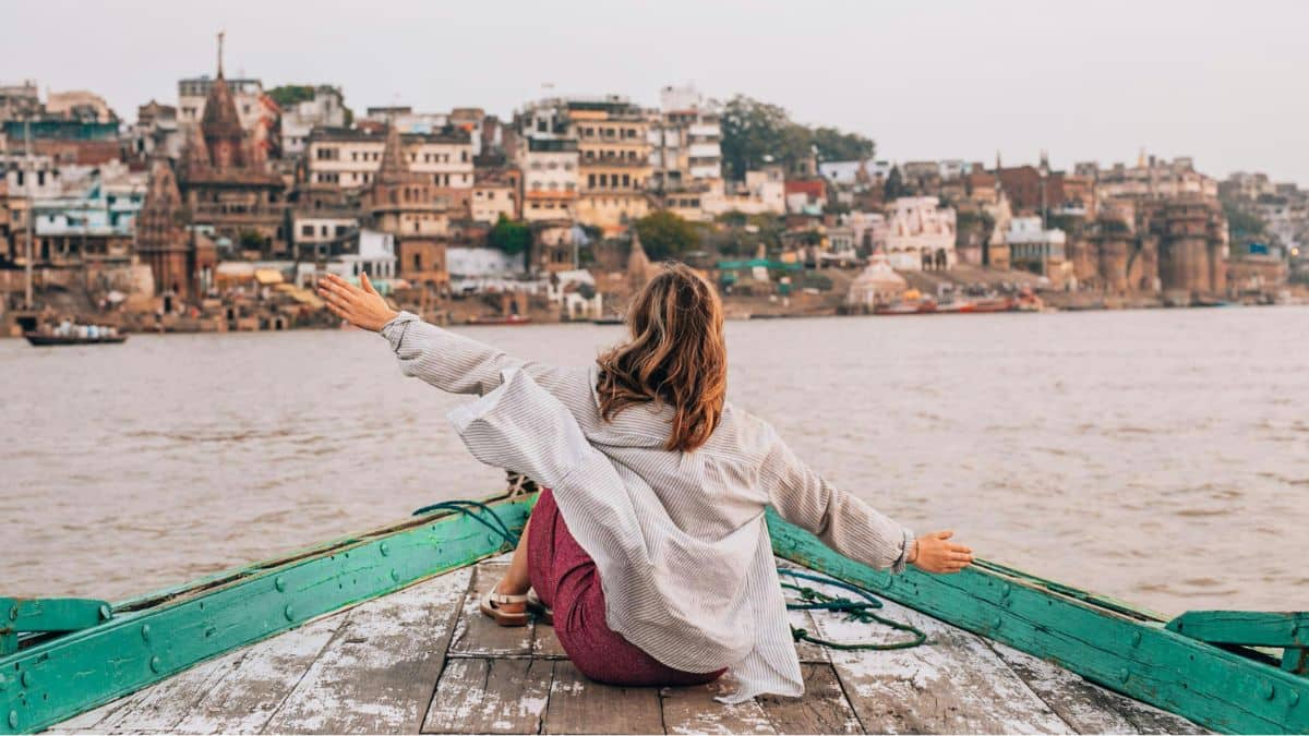 A solo woman with outstretched arms on a boat in Varanasi, illustrating the positive answer to 'Is India safe for solo female travelers?' when practicing smart Varanasi safety for women tips like modest dress.