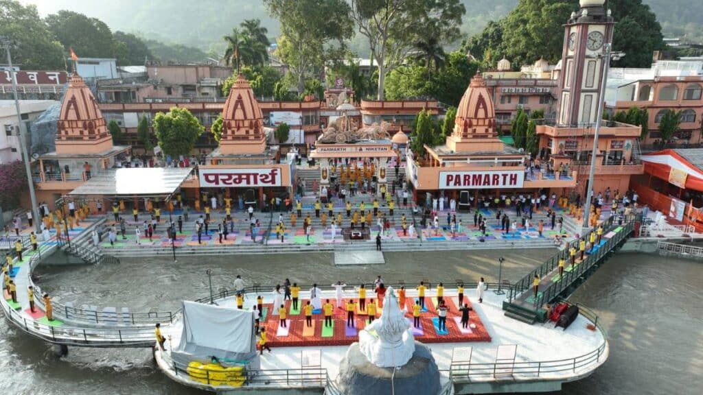 Aerial view of Parmarth Niketan ashram in Rishikesh featuring the Shiva statue and a group yoga session on the Ganga ghats.