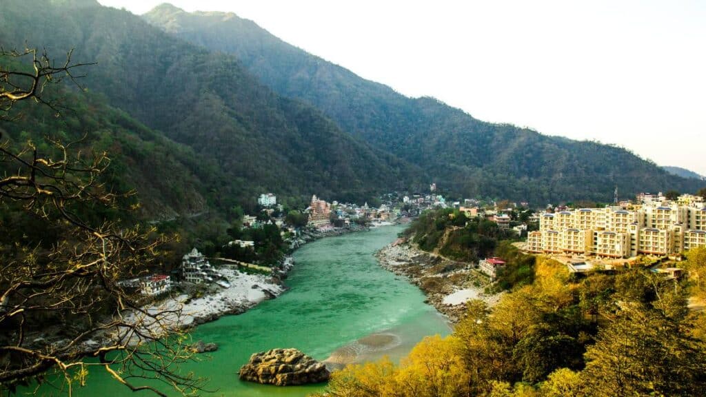 Wide-angle landscape of Rishikesh 2026 showing the Ganga river, spiritual ashrams, and the Himalayan foothills at sunset.