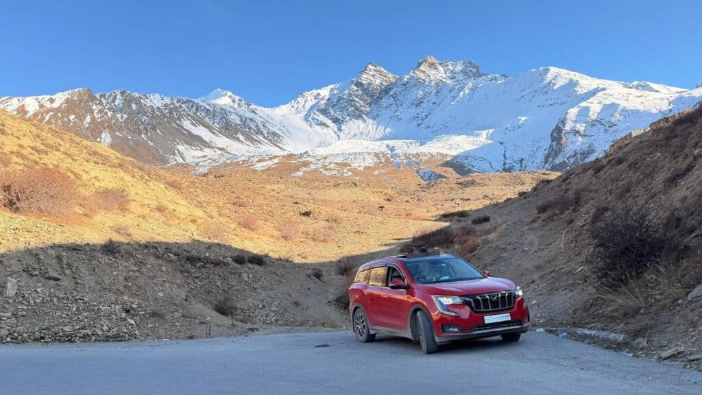 A red SUV parked on a rugged dirt road against a backdrop of snow-capped Himalayan mountains, representing an adventurous India road trip that requires essential packing gear.